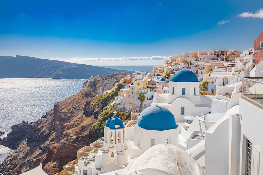 A coastal town with white buildings and blue domes, overlooking the sea and a mountainous backdrop. 3