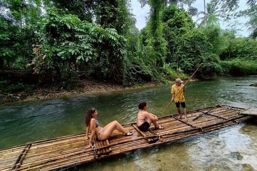 A river with a bamboo raft, two people sitting, and one person standing. 3
