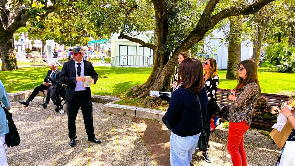 A group of people gathered in a park with trees and a white building in the background. 4