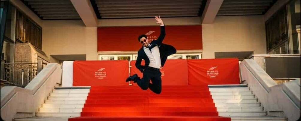 A person jumping down a set of stairs with red carpet and a banner that reads 'Cannes Film Festival.' 1