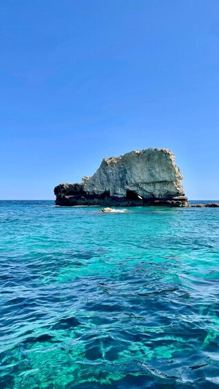 A clear blue sea with a rocky outcrop in the distance. 3