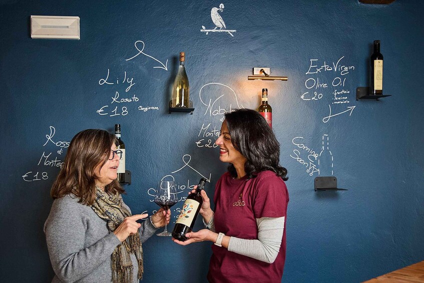 Two people holding wine bottles in front of a wall with wine-related drawings and labels. 5