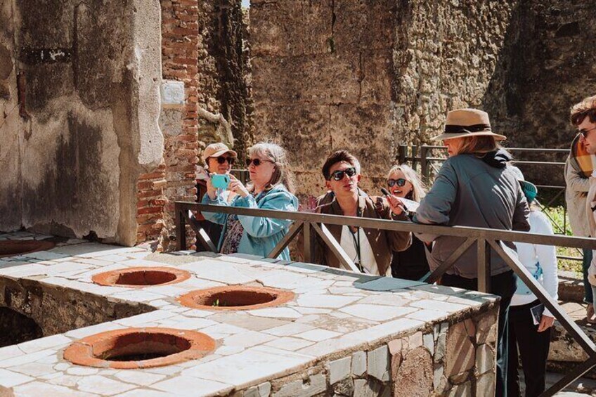 People observing ancient ruins with stone structures and circular openings. 2