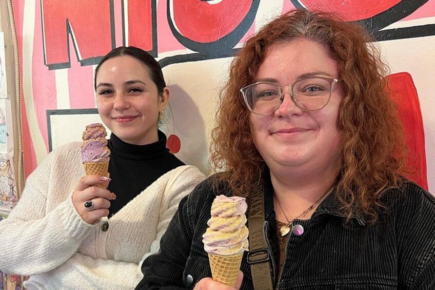 Two people holding ice cream cones in front of a wall with large letters. 5