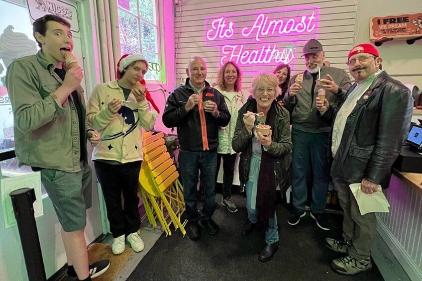 A group of people in a brightly lit indoor setting with a neon sign that reads 'It's Almost Healthy.' 1
