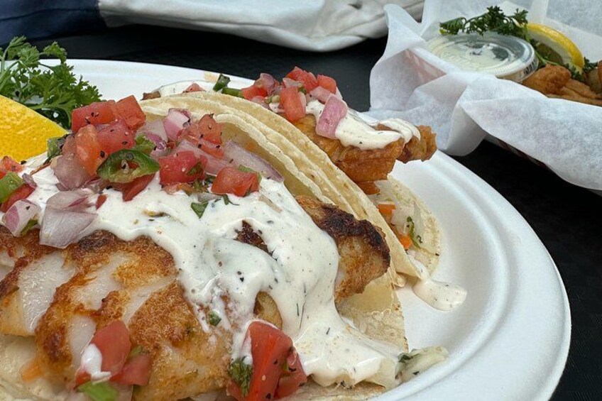A plate with fish tacos, a lemon wedge, and a side of tartar sauce. 4