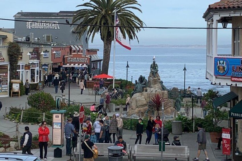 A coastal promenade with shops, a statue, and a view of the sea. 4