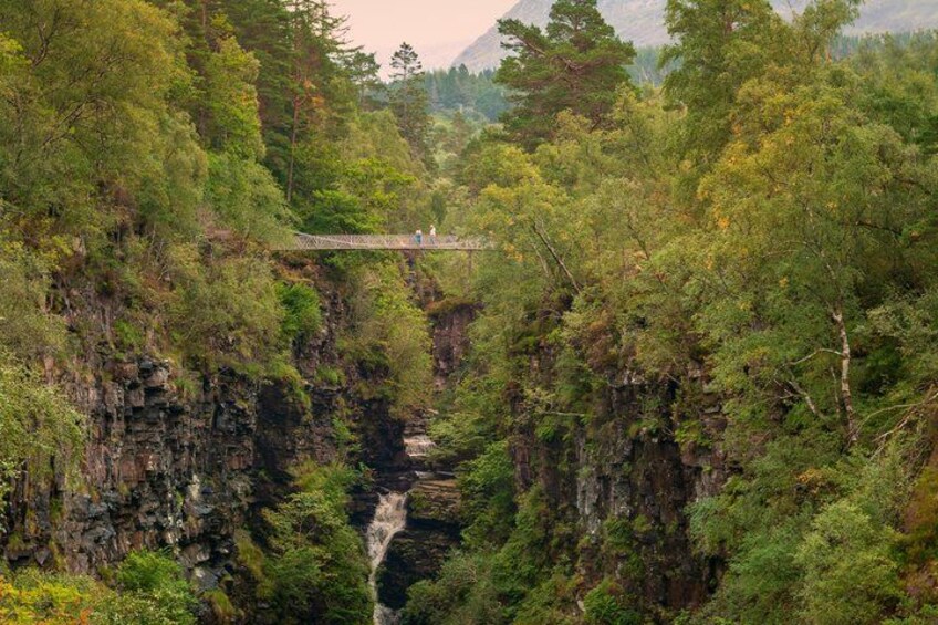 Een hangbrug boven een canyon met dicht bos en rotsachtige kliffen. 1