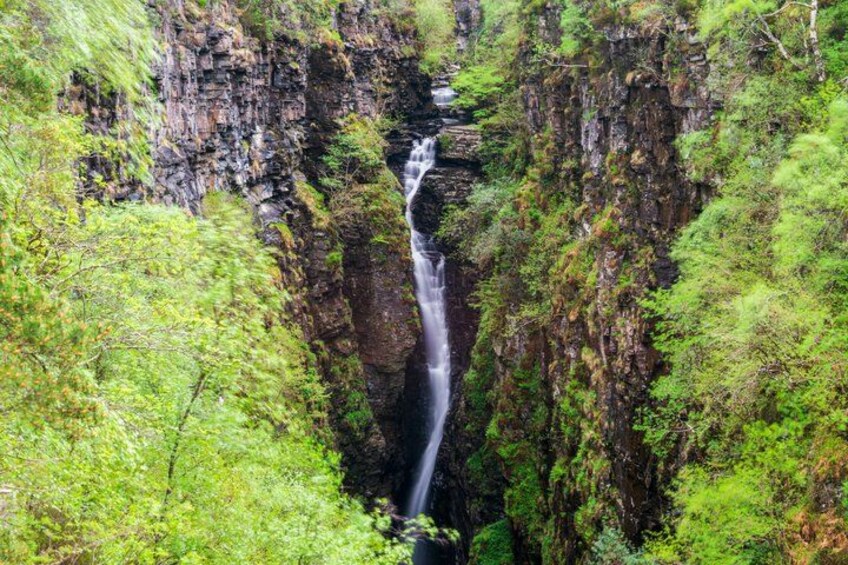 Et vandfald styrter ned ad en klippe omgivet af frodig vegetation. 3