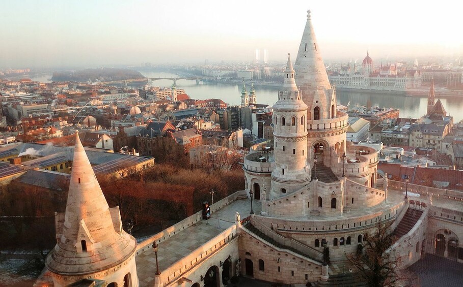 A historic castle with multiple towers, surrounded by a cityscape with a river and bridges in the background. 1
