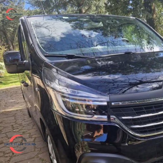 A black SUV parked on a paved path with trees in the background. 1