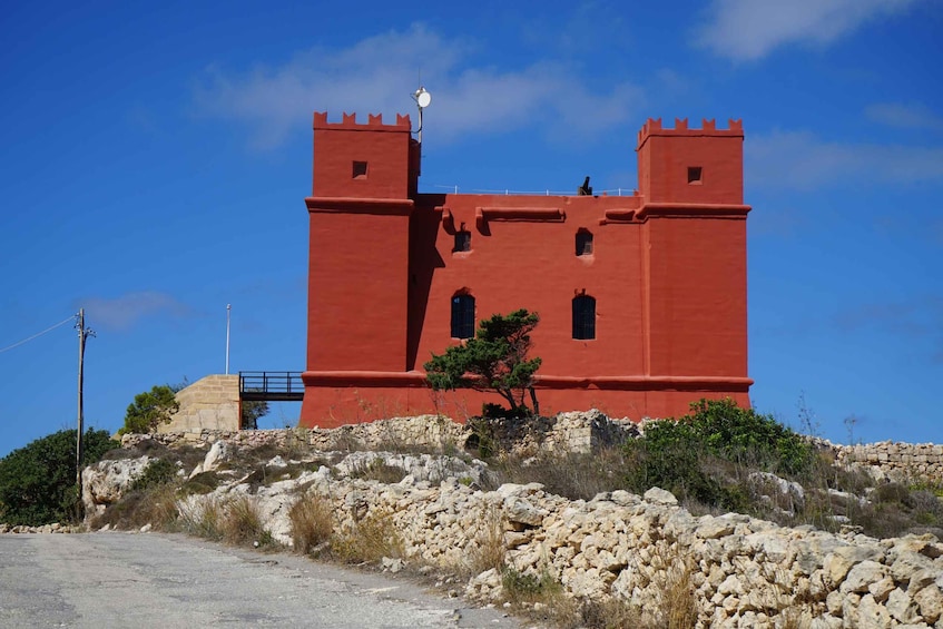 A red castle-like structure with two towers, a small tree in front, and rocky terrain. 4