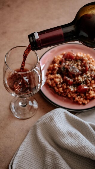 Una botella vertiendo líquido rojo en un vaso, un plato de comida y un paño. 2
