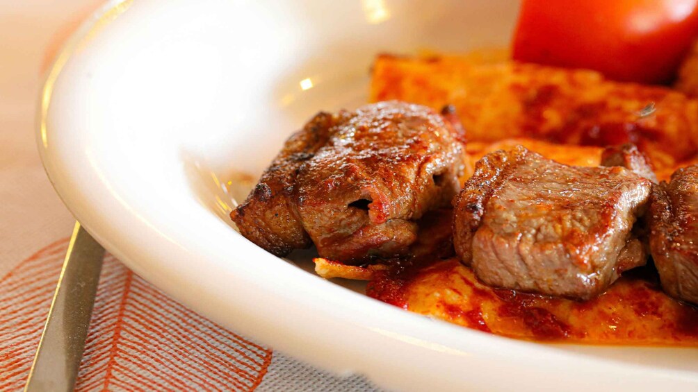 A bowl of cooked meat with a red sauce, possibly beef, on a white plate. 1