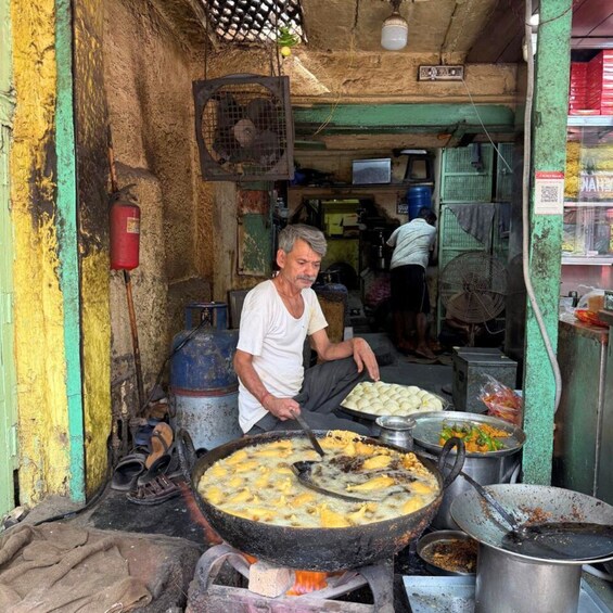 A street food vendor cooking at an outdoor stall with large pots and a fan above. 5