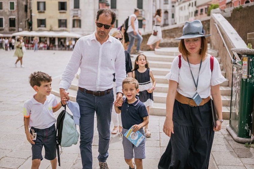 A man and woman walking with two children, holding hands, in an urban setting with buildings and steps. 1
