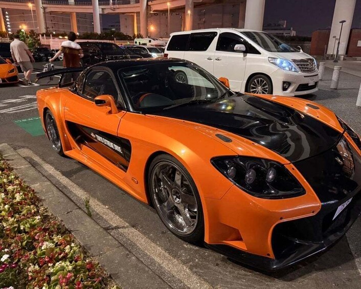 A bright orange sports car parked in a lot with other vehicles, including a white van and a black car. 3