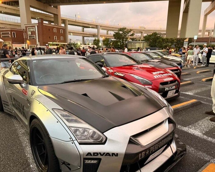 A row of sports cars parked in a lot with a crowd of people in the background. 2