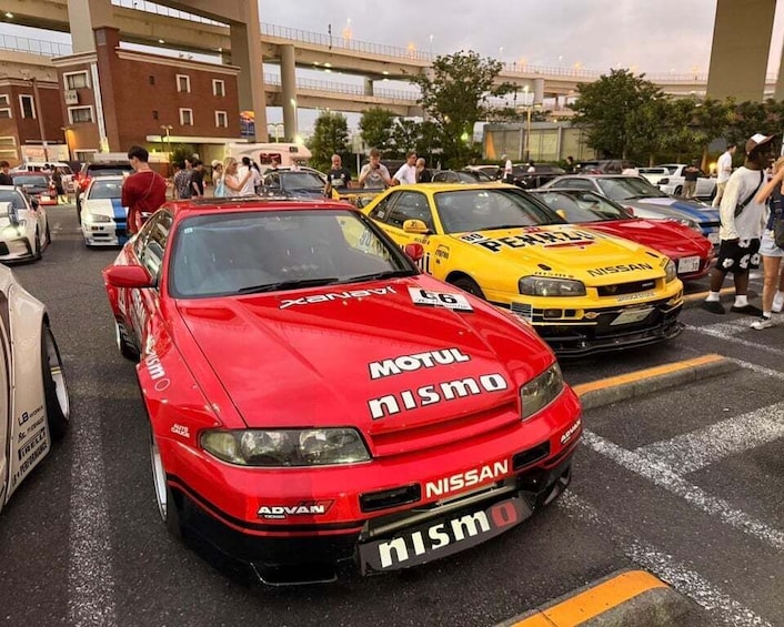 A red Nissan with 'Motul Nismo' and 'ADVAN' decals parked in a lot with other cars. 4