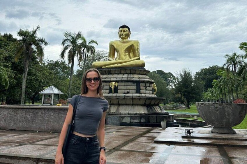 Una gran estatua dorada de Buda en un parque con palmeras y un pequeño pabellón al fondo. 5