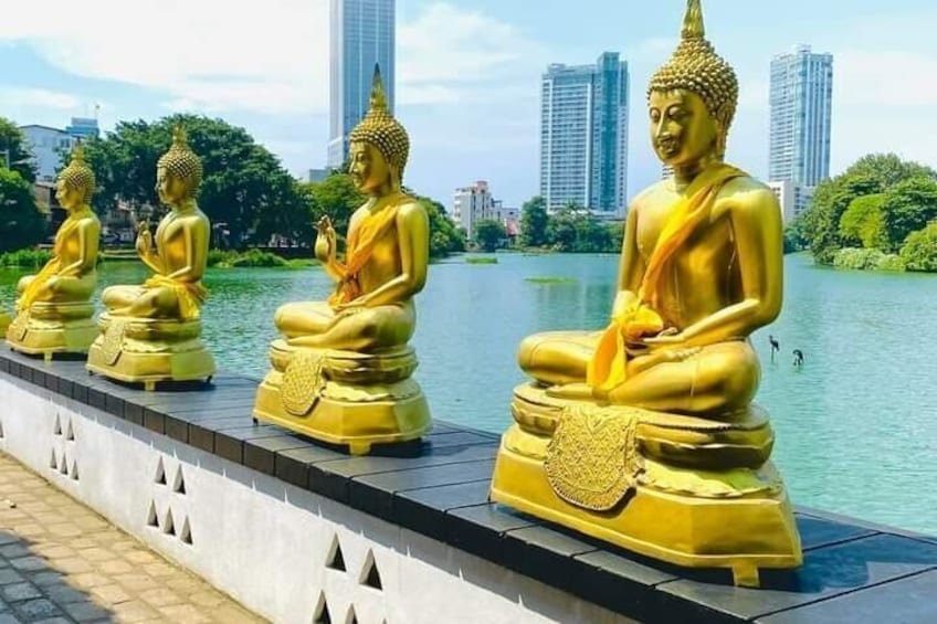 Estatuas doradas de Buda alineadas a lo largo de un paseo fluvial, con un paisaje urbano al fondo. 1