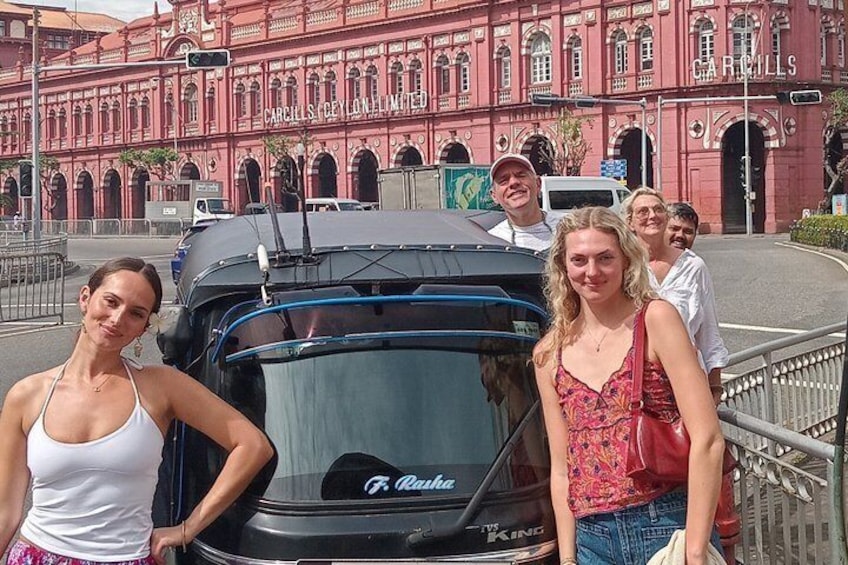 Un grupo de personas frente a un edificio rojo con ventanas de arco y el nombre 1