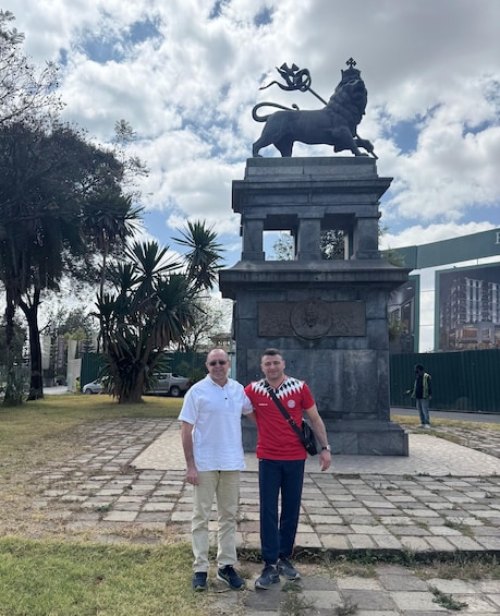Two people standing in front of a statue of a lion on a pedestal. 1