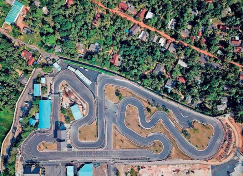 An aerial view of a winding race track surrounded by dense greenery and residential buildings. 3