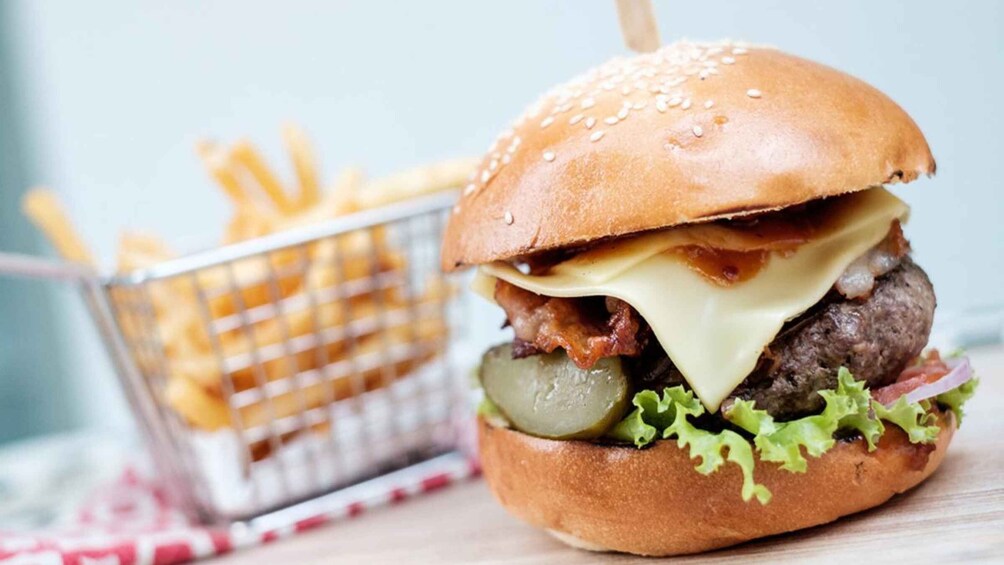A burger with lettuce, cheese, bacon, and pickles on a bun, accompanied by a basket of fries. 2
