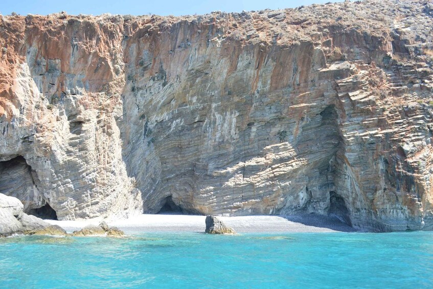 A coastal cliff with a cave entrance and a small rock formation in the water. 4