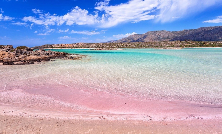 A beach with clear turquoise water, a pink sand shore, and rocky outcrops in the background. 2