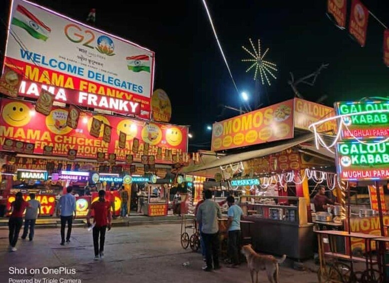 A busy street at night with brightly lit signs for various food vendors. 5