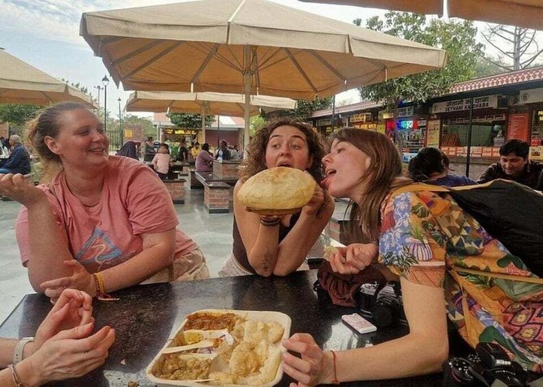 Three people at an outdoor dining area with umbrellas and food containers. 2