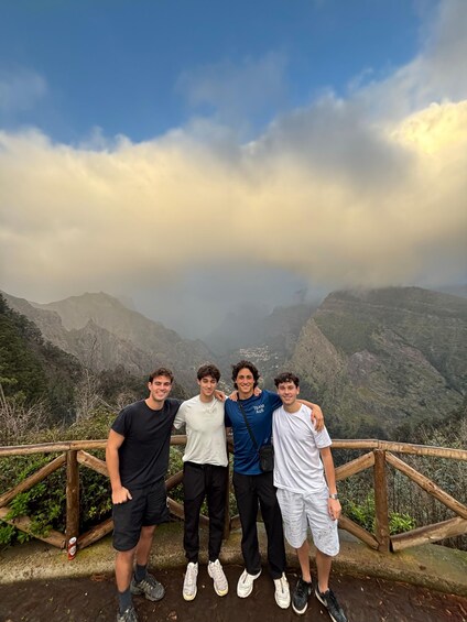 Four people standing on a wooden platform with a mountainous landscape in the background. 1