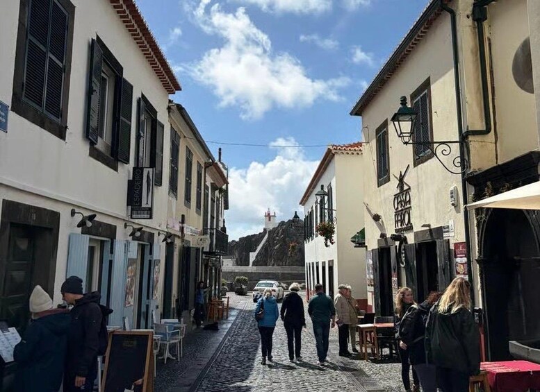 A cobblestone street lined with buildings, a few people walking, and a mountain in the background. 5