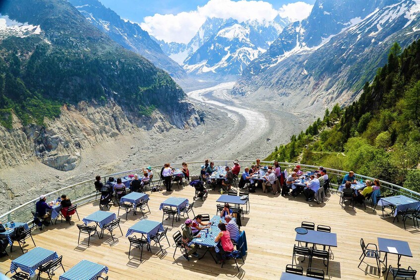 A scenic outdoor dining area with tables and chairs overlooking a glacier and mountains. 4