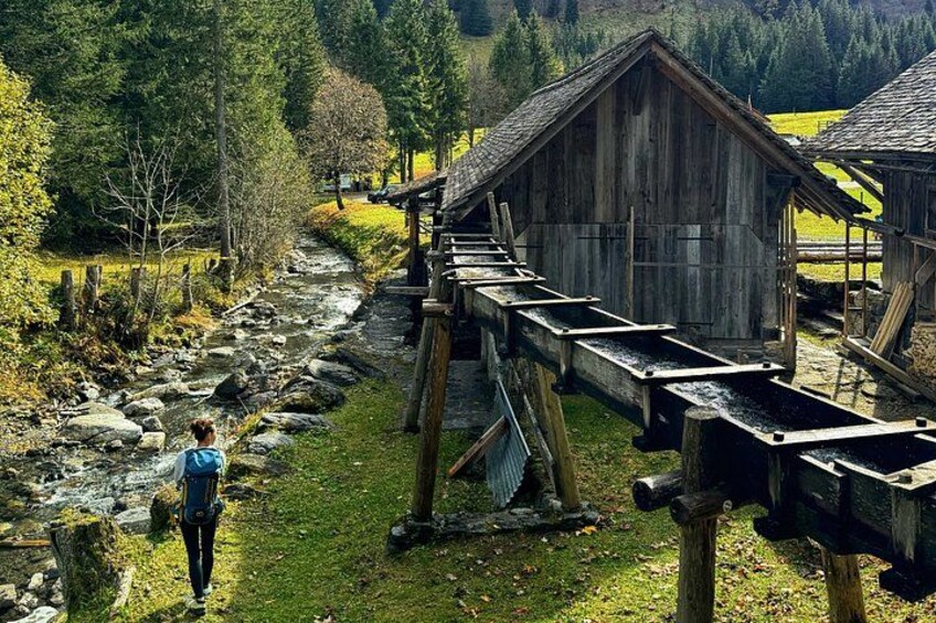 Un pont en bois enjambant un ruisseau, une personne se tenant sur le pont et un bâtiment en bois en arrière-plan. 2