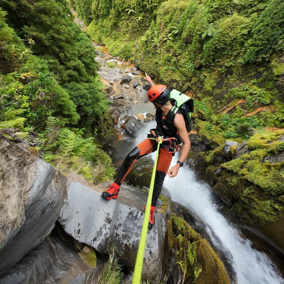 A person rappelling down a rocky cliff with a flowing waterfall in the background. 5