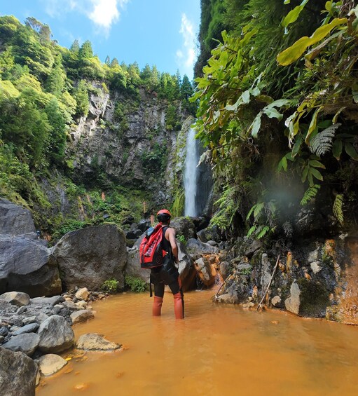A hiker in a forested area with a waterfall and a muddy stream. 4