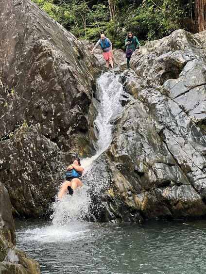 A waterfall in a rocky area with people climbing and sliding down. 1