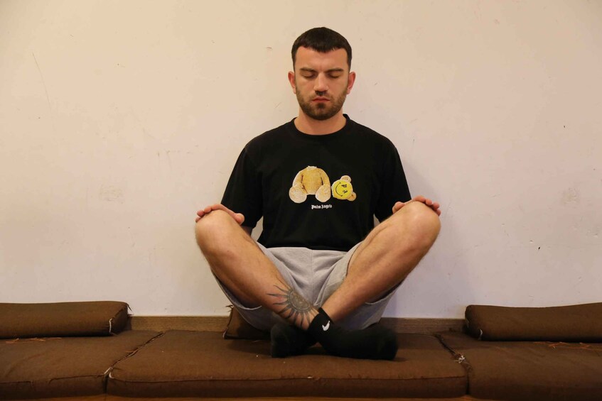 A person sitting cross-legged on a brown couch against a plain wall. 4