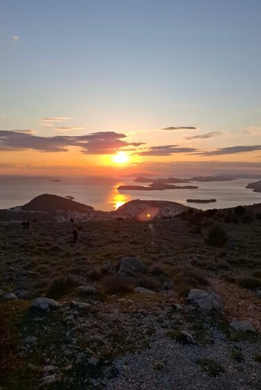 Auringonlasku rannikkomaisemassa, jossa on kallioista maastoa ja muutama kävelevä ihminen. 5