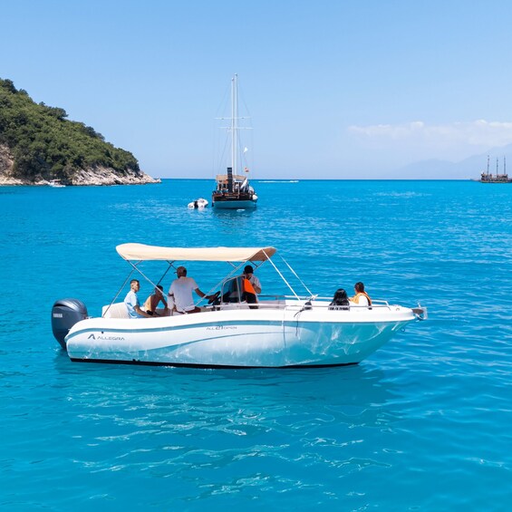 A white boat with people on it, a larger sailboat in the background, and a rocky coastline. 2