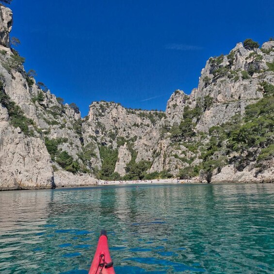 A red kayak on calm turquoise water with rocky cliffs and sparse vegetation in the background. 2