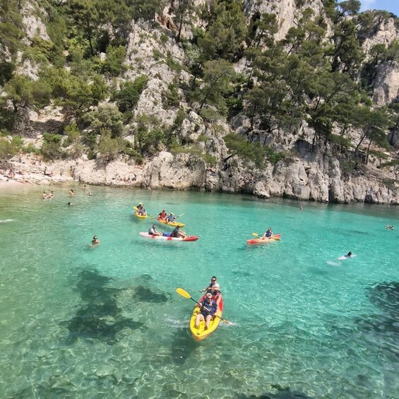 People kayaking on a clear turquoise sea with rocky cliffs in the background. 4