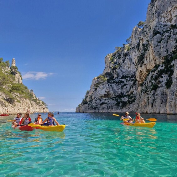 People kayaking in clear waters with rocky cliffs and a lighthouse in the background. 1