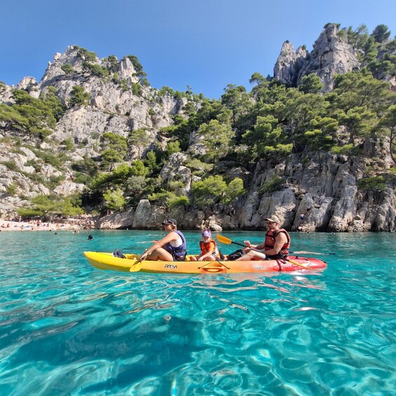 Three people kayaking on a turquoise sea with rocky cliffs in the background. 4