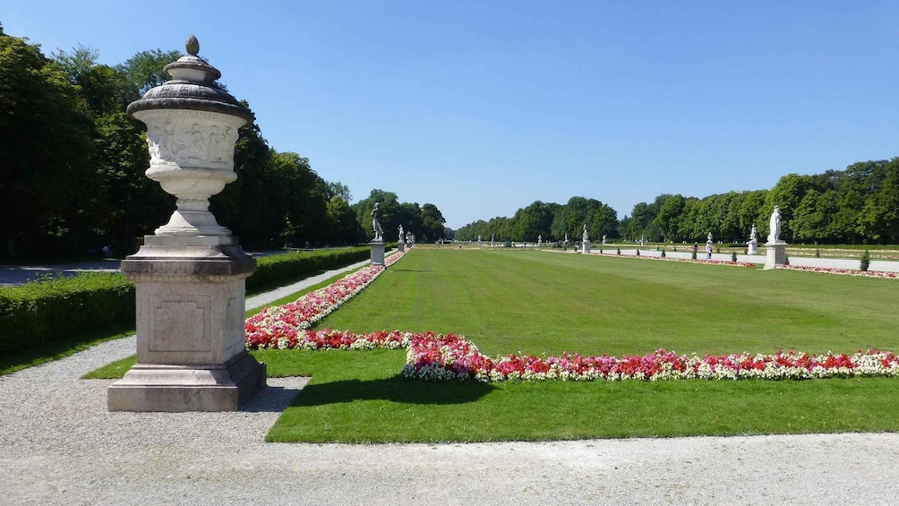 A formal garden with a central lawn, flower beds, and statues. 2