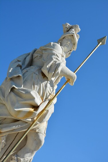 A statue of a figure holding a spear, set against a clear blue sky. 3