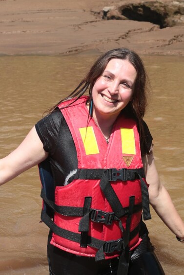 A person wearing a red life jacket with yellow reflective patches, standing in shallow water. 5